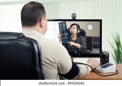 Middle-aged Man Measures His Blood Pressure In Front Of Virtual Doctor. In The Meantime, Telemedicine Physician Is Carefully Looking At His Brain X Ray Picture In The Monitor. Horizontal Shot