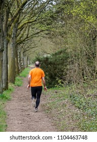 Middle-aged Man In Orange T-shirt And Black Spandex Tights Running Through Woodland In Bois De Vincennes, Paris