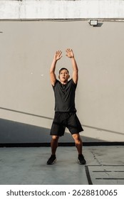 A middle-aged man performs jumping jacks outdoors against a concrete wall during a high-intensity workout session just outside the gym.