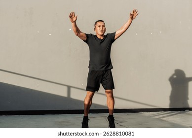 A middle-aged man performs jumping jacks outdoors against a concrete wall during a high-intensity workout session just outside the gym.