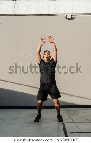 A middle-aged man performs jumping jacks outdoors against a concrete wall during a high-intensity workout session just outside the gym.