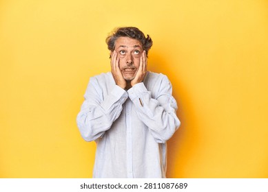 Middle-aged man posing on a yellow backdrop whining and crying disconsolately.