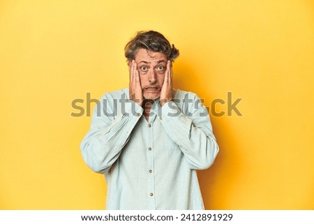 Middle-aged man posing on a yellow backdrop whining and crying disconsolately.