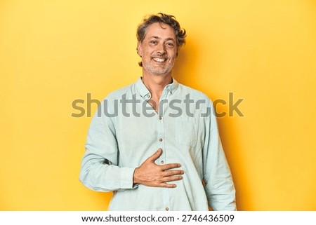 Middle-aged man posing on a yellow backdrop touches tummy, smiles gently, eating and satisfaction concept.
