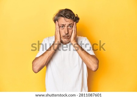 Middle-aged man posing on a yellow backdrop crying, unhappy with something, agony and confusion concept.