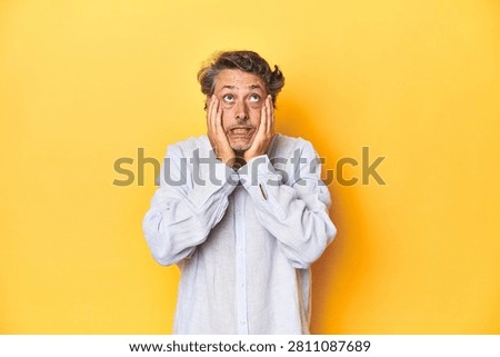 Middle-aged man posing on a yellow backdrop whining and crying disconsolately.