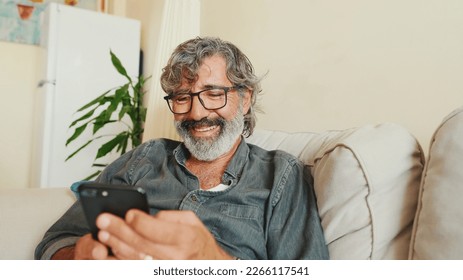 Middle-aged man relaxing on his couch while in home and using his smartphone to text - Powered by Shutterstock