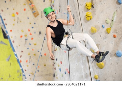 Middle-aged man in safety helmet and with safety rope hangs near climbing wall in gym. active hobby concept - Powered by Shutterstock