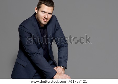 A middle-aged man is sitting, leaning forward, in an expensive suit against the gray background of the studio, cruelly, manfully