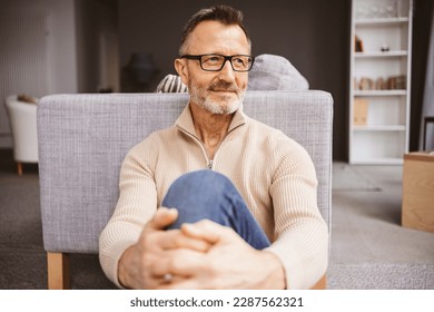 Middle-aged man sitting on living room floor and looking to the side - Powered by Shutterstock