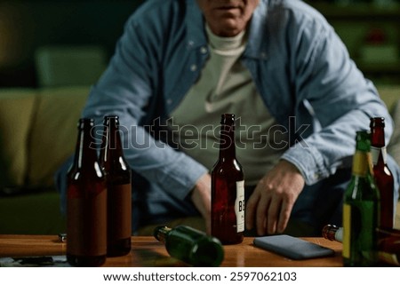Middle-aged man sitting at table with several alcoholic beverages looking pensive and reflecting in dimly lit room background