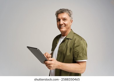 Middle-aged man smiles while using tablet in neutral studio setting for digital communication