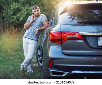 A middle-aged man is standing near the car. Muccina speaks on the phone. Dear beautiful car. The man is calm and confident. The car is in the summer park. A man speaks on the phone near his car. - Shutterstock ID 2181634079