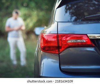A middle-aged man is standing near the car. Muccina speaks on the phone. Dear beautiful car. The man is calm and confident. The car is in the summer park.