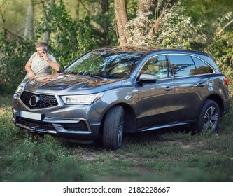 A middle-aged man is standing near the car. Muccina speaks on the phone. Dear beautiful car. The man is calm and confident. The car is in the summer park.