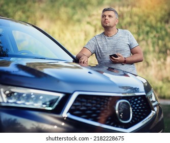 A middle-aged man is standing near the car. Muccina speaks on the phone. Dear beautiful car. The man is calm and confident. The car is in the summer park.