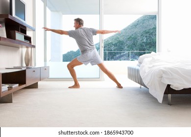 Middle-aged man stretching while doing yoga in his bedroom on a bright, sunny morning - Powered by Shutterstock