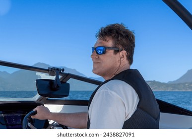 Middle-aged man with sunglasses driving a boat on a summer day at the lake. - Powered by Shutterstock