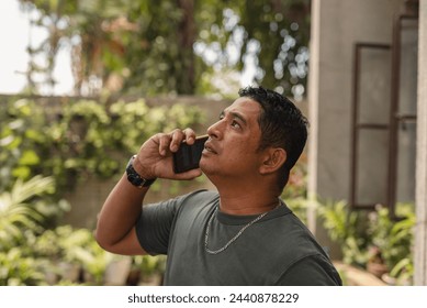 Middle-aged man talking on the phone with a pensive look in a sunny garden setting - Powered by Shutterstock