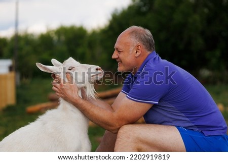 a middle-aged man talks to a white goat face to face and smiles