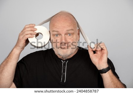 Middle-Aged Man with Toilet Paper Roll as Over or Under Concept on Grey Background