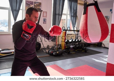 Middle-aged man training with red boxing bag wearing boxing gloves in indoor gym facility