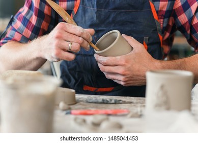 A middle-aged man in a uniform work by wooden stack with a clay shape of cup in a large creative pottery manufacture. Artwork and handmade concept. - Powered by Shutterstock