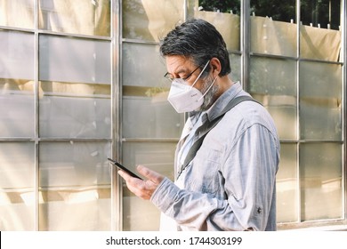 A middle-aged man wearing a KN95 (or FFP2) face mask consults his mobile as he walks past aehead the window of a closed business.  - Powered by Shutterstock