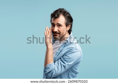 Middle-aged man whispering a secret while sharing gossip or news, displaying a serious expression on his face. Isolated in a studio setting with a light blue background. Advertisement concept