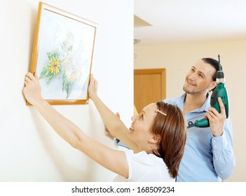 Middle-aged Man And Woman  Hanging  Art Picture In Frame On Wall At Home  