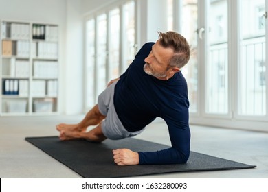 Middle-aged man working out doing side stretches on a mat at the gym in a healthy active lifestyle and fitness concept