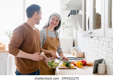 Middle-aged mature happy family couple wife and husband cooking vegetable salad together in the kitchen, helping with preparing food meal. Togetherness and vegetarian lifestyle. - Powered by Shutterstock