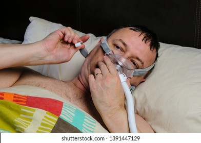 A Middle-aged, Overweight Man Adjusts A CPAP Mask Before Going To Sleep