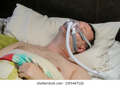 A Middle-aged, Overweight Man Wearing A CPAP Mask While Sleeping In Bed