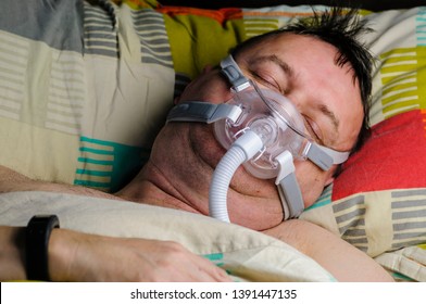 A Middle-aged, Overweight Man Wearing A CPAP Mask While Sleeping In Bed