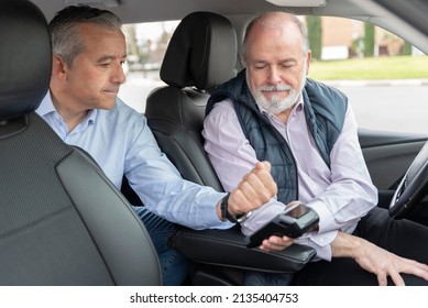 middle-aged passenger in back seat paying with app on watch to elderly driver-concept of transportation, cab, taxi and technology