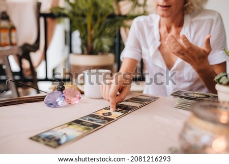 Middle-aged professional tarologist having session. Woman holding tarot cards and speaking with customer about his life
