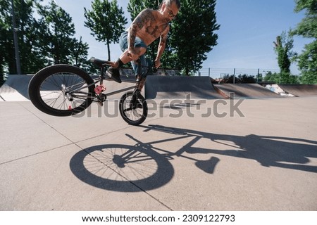 A middle-aged shirtless urban man is performing freestyle tricks and stunts on his bmx in a skate park. A professional extreme sports rider is doing stunts and freestyle tricks in an urban exterior. Stock photo © 