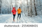 Middle-aged smiling trail couple runners man and woman dressed bright windproof jackets running speaking picturesque snowy forest during sunny frosty day. Sporty active people, winter training image.