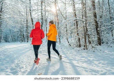 Middle-aged smiling trail couple runners man and woman dressed bright windproof jackets running speaking picturesque snowy forest during sunny frosty day. Sporty active people, winter training image. - Powered by Shutterstock