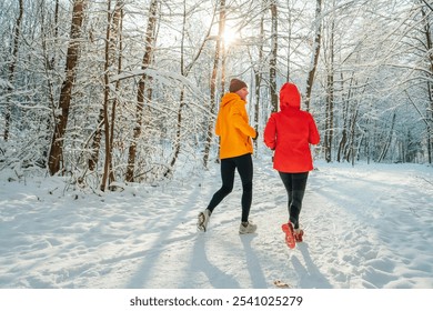 Middle-aged smiling trail couple runners man and woman dressed bright windproof jackets running speaking picturesque snowy forest during sunny frosty day. Sporty active people, winter training image. - Powered by Shutterstock