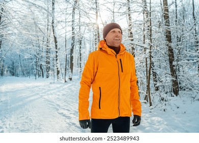 Middle-aged smiling trail runner man dressed bright orange windproof jacket endurance running picturesque snowy forest. Sporty active people and winter training concept image. - Powered by Shutterstock