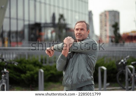 A middle-aged sportsman doing stretching exercises in an urban area.