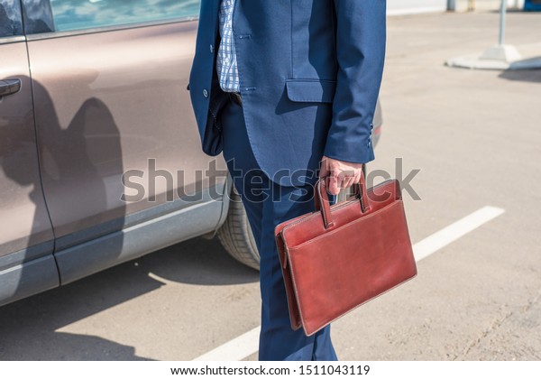 Middle-aged  tall\
gray-haired businessman in blue suit with brown briefcase walks to\
his car on the private\
parking