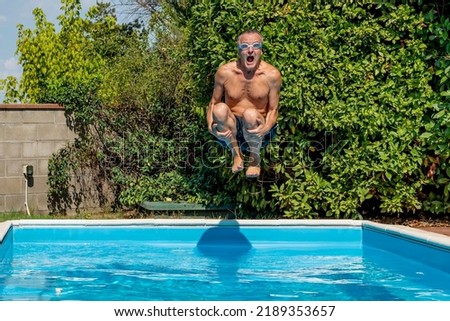 Middle-aged white man with a funny expression dives into the pool with swimming goggles, cannonball style