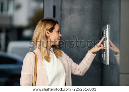 A middle-aged woman is calling intercom on a building downtown.