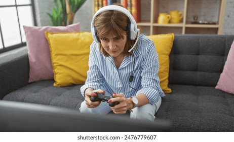 A middle-aged woman in casual attire enjoys gaming with a controller and headphones in a cozy living room. - Powered by Shutterstock