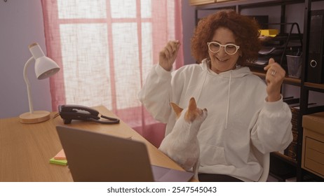 Middle-aged woman dancing with her chihuahua in a home office setting, with the dog standing on her lap, smiling in a cozy indoor environment filled with office accessories. - Powered by Shutterstock