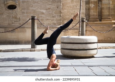 Middle-aged woman doing the yoga pose sirsasana, headstand. She is on the street between the streetcar rails on a large avenue in a city. Concept of health and sport.