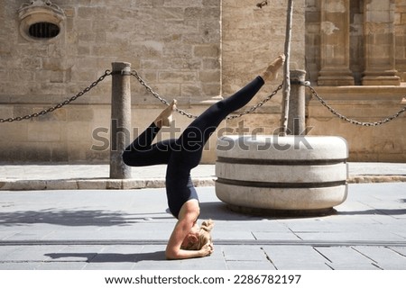Middle-aged woman doing the yoga pose sirsasana, headstand. She is on the street between the streetcar rails on a large avenue in a city. Concept of health and sport.